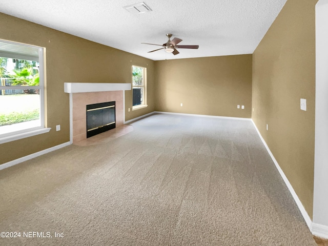 unfurnished living room with ceiling fan, a healthy amount of sunlight, a textured ceiling, and a tiled fireplace