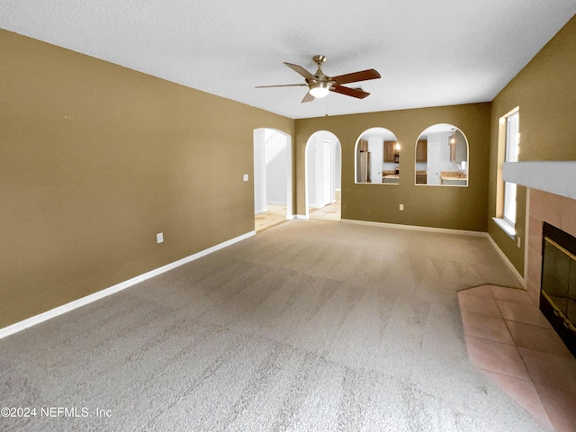 unfurnished living room featuring a tile fireplace, light carpet, a textured ceiling, and ceiling fan