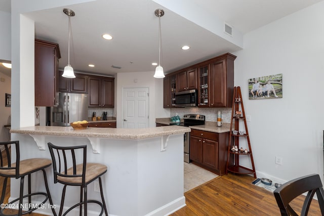 kitchen with pendant lighting, a kitchen breakfast bar, light wood-type flooring, and stainless steel appliances