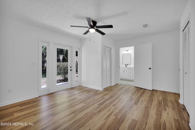 unfurnished bedroom with ensuite bath, ceiling fan, access to exterior, a textured ceiling, and light hardwood / wood-style floors