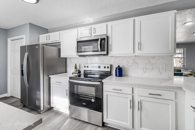 kitchen featuring white cabinets, light wood-type flooring, appliances with stainless steel finishes, and tasteful backsplash