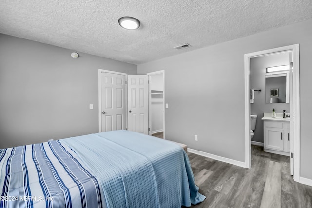 bedroom with a textured ceiling, dark hardwood / wood-style flooring, ensuite bathroom, and a closet