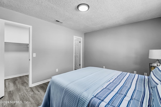 bedroom with wood-type flooring, a textured ceiling, a spacious closet, and a closet