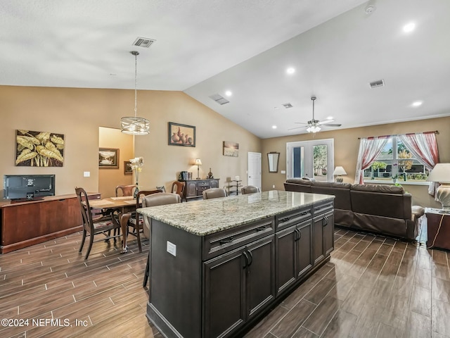 kitchen featuring light stone countertops, dark hardwood / wood-style flooring, vaulted ceiling, pendant lighting, and a kitchen island