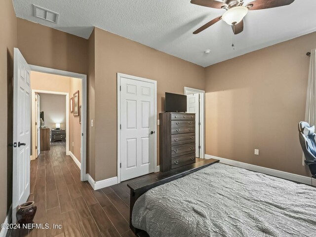 bedroom with ceiling fan, dark hardwood / wood-style flooring, and a textured ceiling