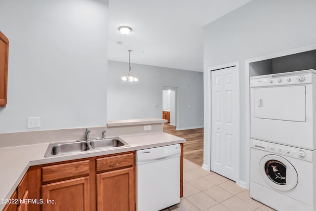 kitchen with white dishwasher, sink, an inviting chandelier, stacked washer / dryer, and hanging light fixtures