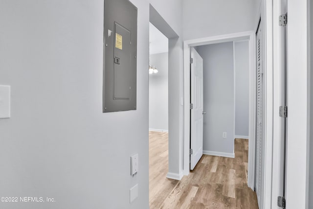 corridor featuring light wood-type flooring, electric panel, and a notable chandelier