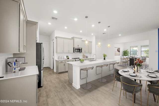 kitchen featuring appliances with stainless steel finishes, decorative light fixtures, sink, a kitchen bar, and light wood-type flooring