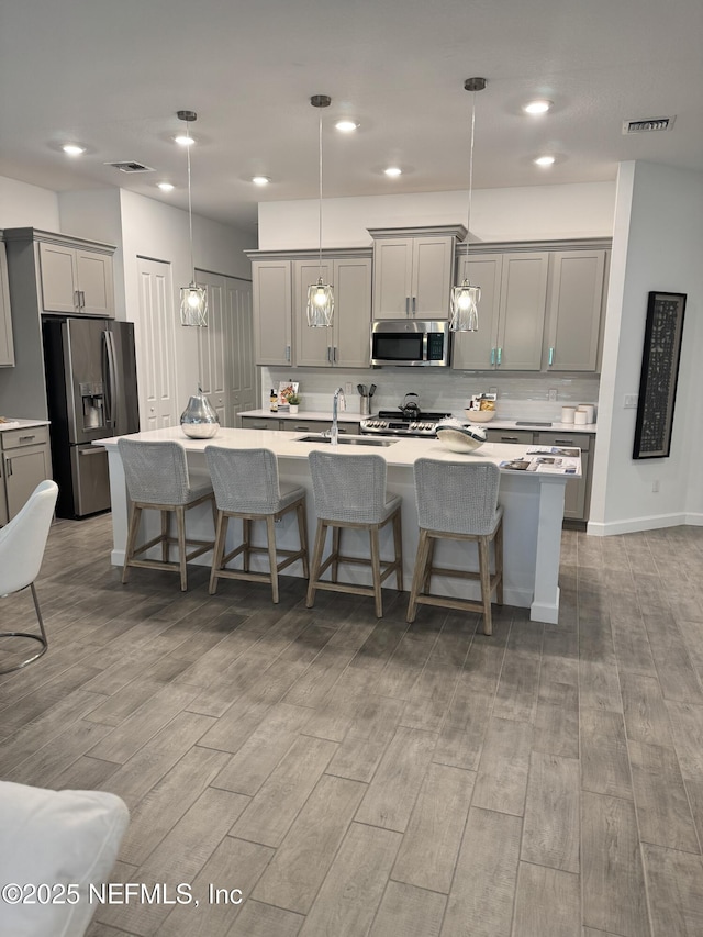 kitchen featuring gray cabinets, appliances with stainless steel finishes, pendant lighting, sink, and a kitchen island with sink