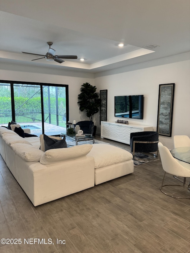 living room with ceiling fan, wood-type flooring, and a raised ceiling