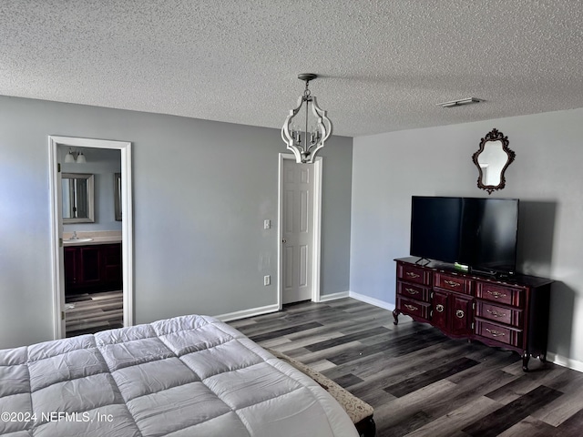 bedroom with ensuite bath, a textured ceiling, dark wood-type flooring, sink, and a chandelier