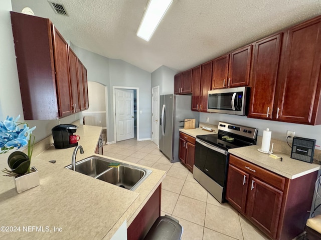 kitchen with sink, vaulted ceiling, a textured ceiling, light tile patterned flooring, and stainless steel appliances