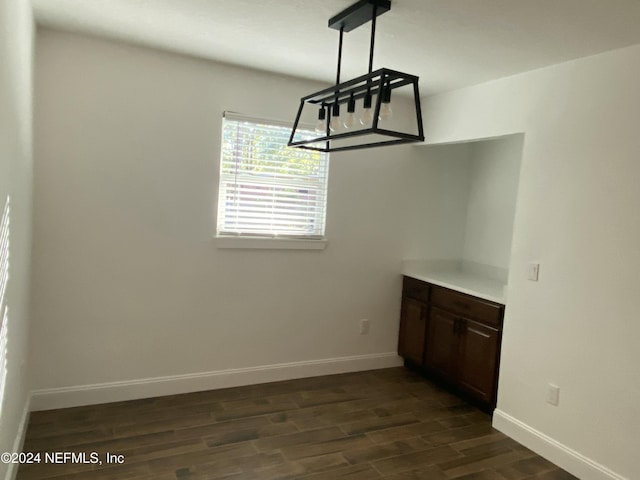 unfurnished dining area with dark wood-type flooring and an inviting chandelier