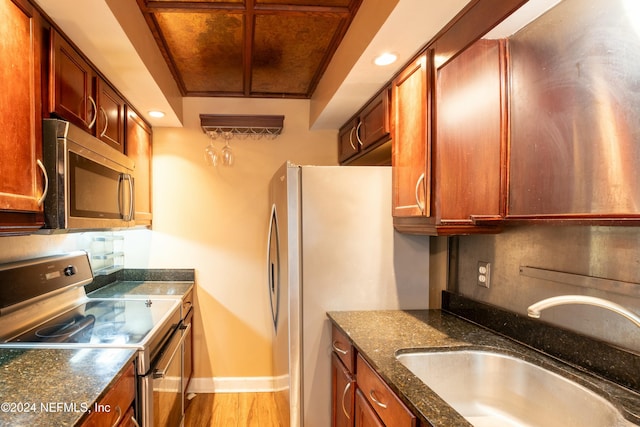 kitchen with appliances with stainless steel finishes, hardwood / wood-style flooring, dark stone counters, and sink