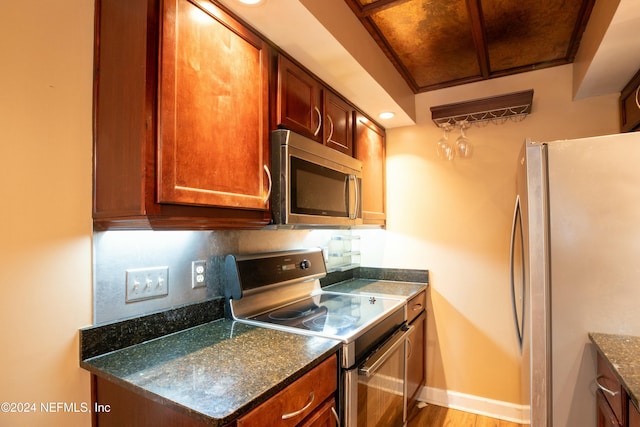 kitchen with light hardwood / wood-style floors, dark stone countertops, and stainless steel appliances