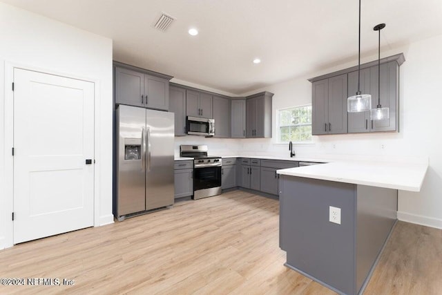 kitchen featuring pendant lighting, gray cabinetry, appliances with stainless steel finishes, light hardwood / wood-style floors, and kitchen peninsula