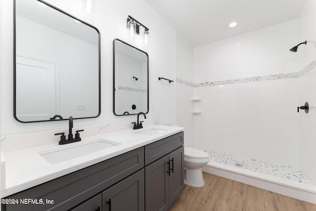 bathroom with hardwood / wood-style flooring, vanity, toilet, and a tile shower