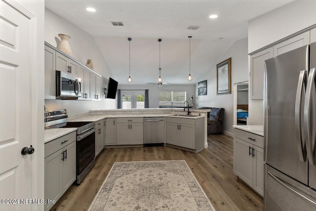 kitchen with pendant lighting, lofted ceiling, kitchen peninsula, and appliances with stainless steel finishes