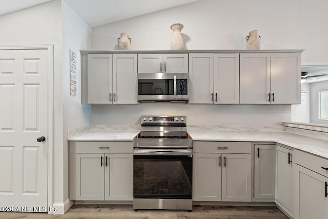 kitchen with appliances with stainless steel finishes, gray cabinetry, vaulted ceiling, ceiling fan, and light hardwood / wood-style flooring