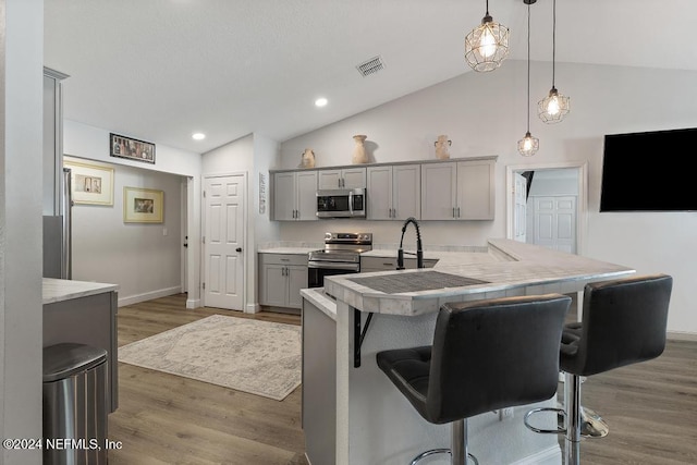 kitchen featuring appliances with stainless steel finishes, gray cabinetry, a breakfast bar, vaulted ceiling, and hanging light fixtures