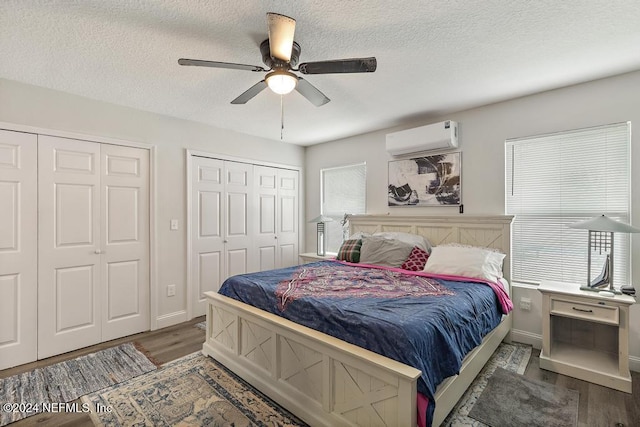 bedroom featuring ceiling fan, dark hardwood / wood-style flooring, an AC wall unit, a textured ceiling, and two closets