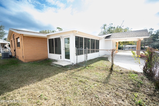 rear view of house featuring a sunroom, central air condition unit, and a lawn