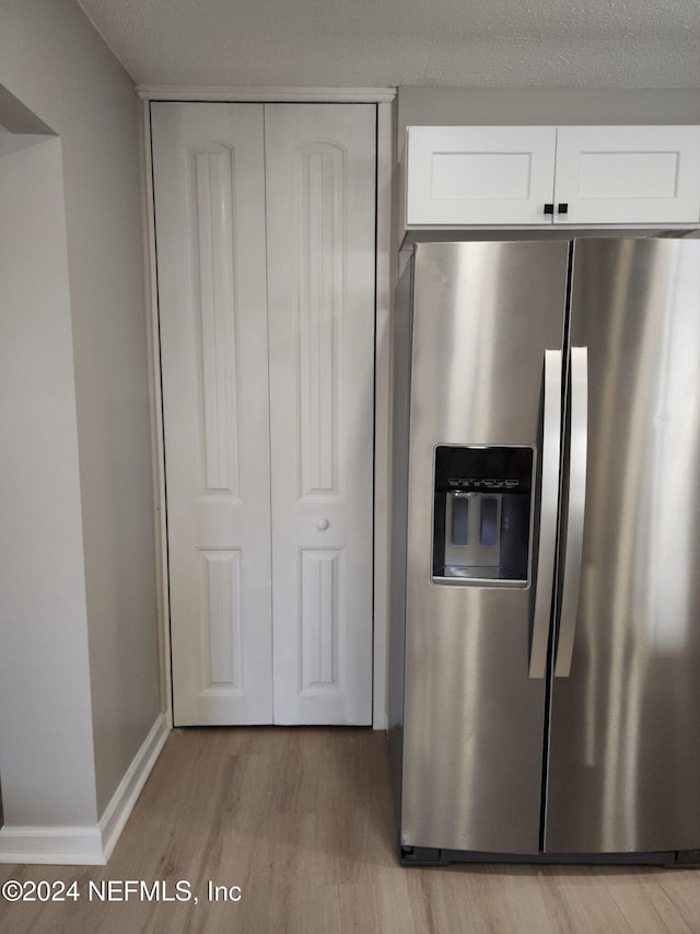 kitchen with stainless steel fridge, a textured ceiling, light hardwood / wood-style floors, and white cabinetry