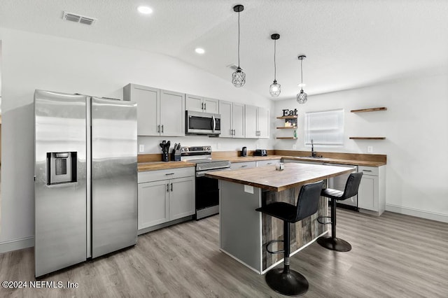 kitchen with pendant lighting, wooden counters, vaulted ceiling, appliances with stainless steel finishes, and a kitchen island