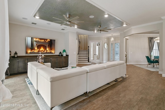 living room with ceiling fan, ornamental molding, a fireplace, and light hardwood / wood-style flooring