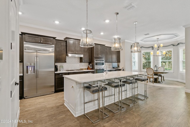 kitchen featuring a breakfast bar area, appliances with stainless steel finishes, dark brown cabinetry, a center island with sink, and decorative light fixtures