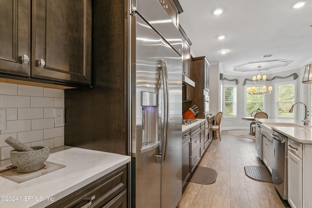 kitchen with sink, crown molding, decorative light fixtures, appliances with stainless steel finishes, and backsplash