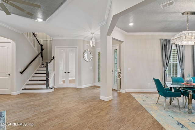 entrance foyer featuring ornamental molding, ceiling fan with notable chandelier, a textured ceiling, and light hardwood / wood-style floors