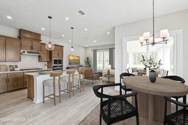 kitchen with pendant lighting, light hardwood / wood-style floors, an inviting chandelier, and a kitchen island with sink