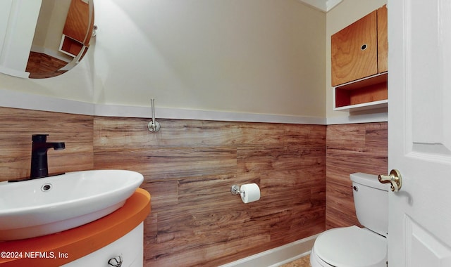 bathroom with wooden walls, vanity, and toilet