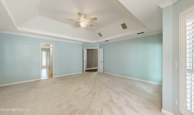 carpeted empty room with a raised ceiling, ceiling fan, and ornamental molding