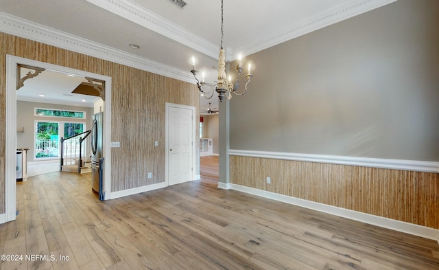 unfurnished room featuring hardwood / wood-style floors, ceiling fan with notable chandelier, ornamental molding, and wood walls