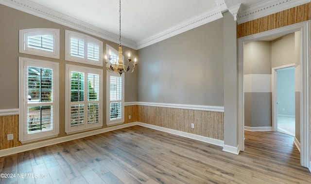 spare room with hardwood / wood-style floors, wood walls, ornamental molding, and a notable chandelier