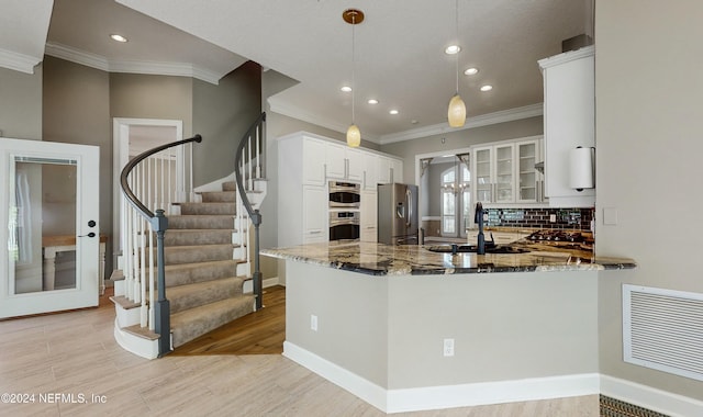 kitchen featuring kitchen peninsula, dark stone countertops, appliances with stainless steel finishes, decorative light fixtures, and white cabinetry