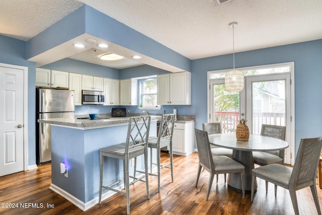 kitchen featuring dark wood-type flooring, white cabinets, hanging light fixtures, a textured ceiling, and stainless steel appliances