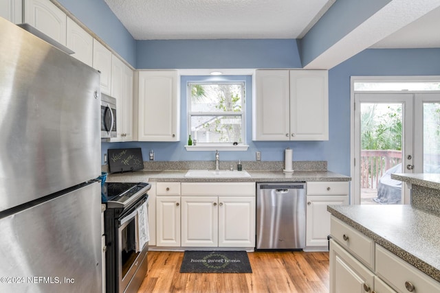 kitchen with appliances with stainless steel finishes, light hardwood / wood-style floors, white cabinetry, and sink