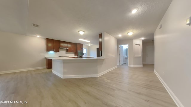 kitchen with kitchen peninsula, a textured ceiling, and light hardwood / wood-style flooring