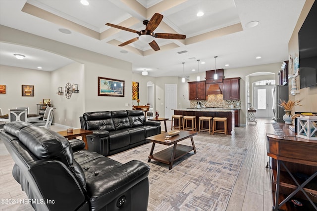 living room featuring ceiling fan, coffered ceiling, beamed ceiling, crown molding, and light hardwood / wood-style floors