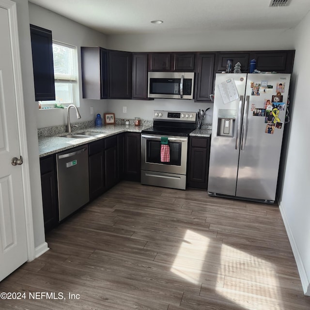 kitchen with hardwood / wood-style flooring, light stone counters, sink, and appliances with stainless steel finishes