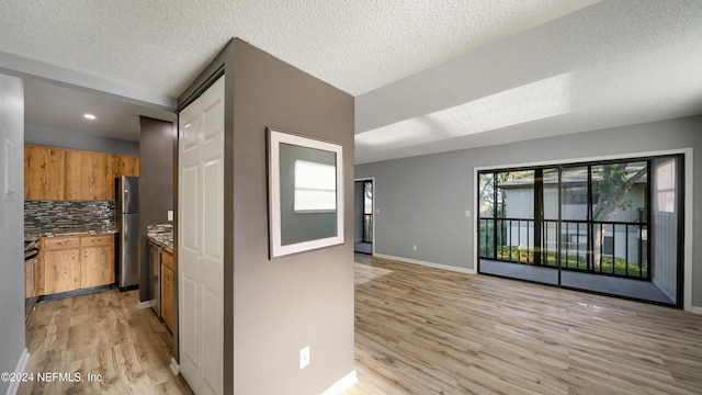 kitchen with backsplash, stainless steel refrigerator, light hardwood / wood-style flooring, and a textured ceiling