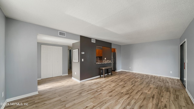 unfurnished living room with a textured ceiling and light wood-type flooring