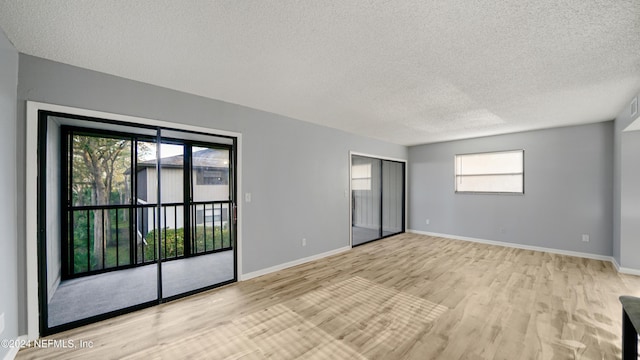 spare room with a textured ceiling, light wood-type flooring, and a healthy amount of sunlight