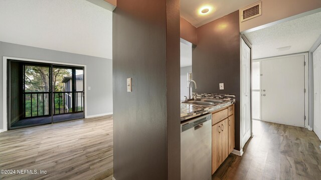 kitchen with light brown cabinetry, stainless steel dishwasher, a textured ceiling, sink, and light hardwood / wood-style floors