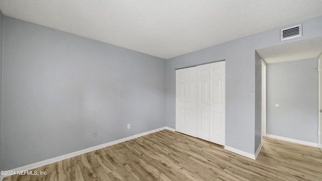 unfurnished bedroom with a textured ceiling, light hardwood / wood-style floors, and a closet