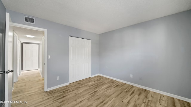 unfurnished bedroom with a textured ceiling, light hardwood / wood-style floors, and a closet