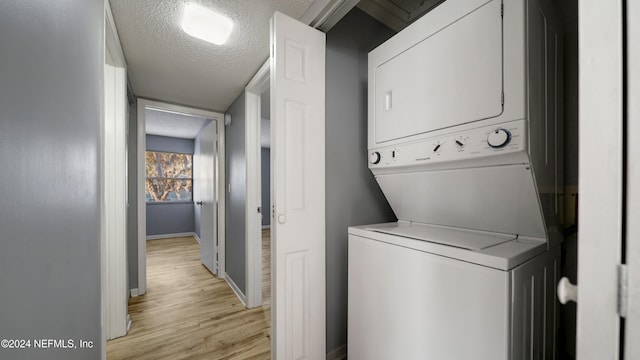 clothes washing area featuring a textured ceiling, light hardwood / wood-style floors, and stacked washer / dryer